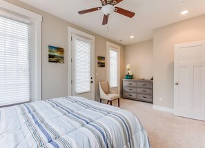 A bedroom with a bed, a ceiling fan, a dresser, and two doors.