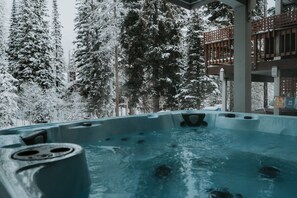 Ett bubbelbad omgivet av snötäckta träd och en träaltan.