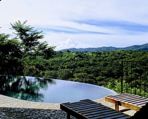 Une piscine à débordement bordée de chaises longues en bois, entourée d’une végétation luxuriante et offrant une vue imprenable sur les montagnes.