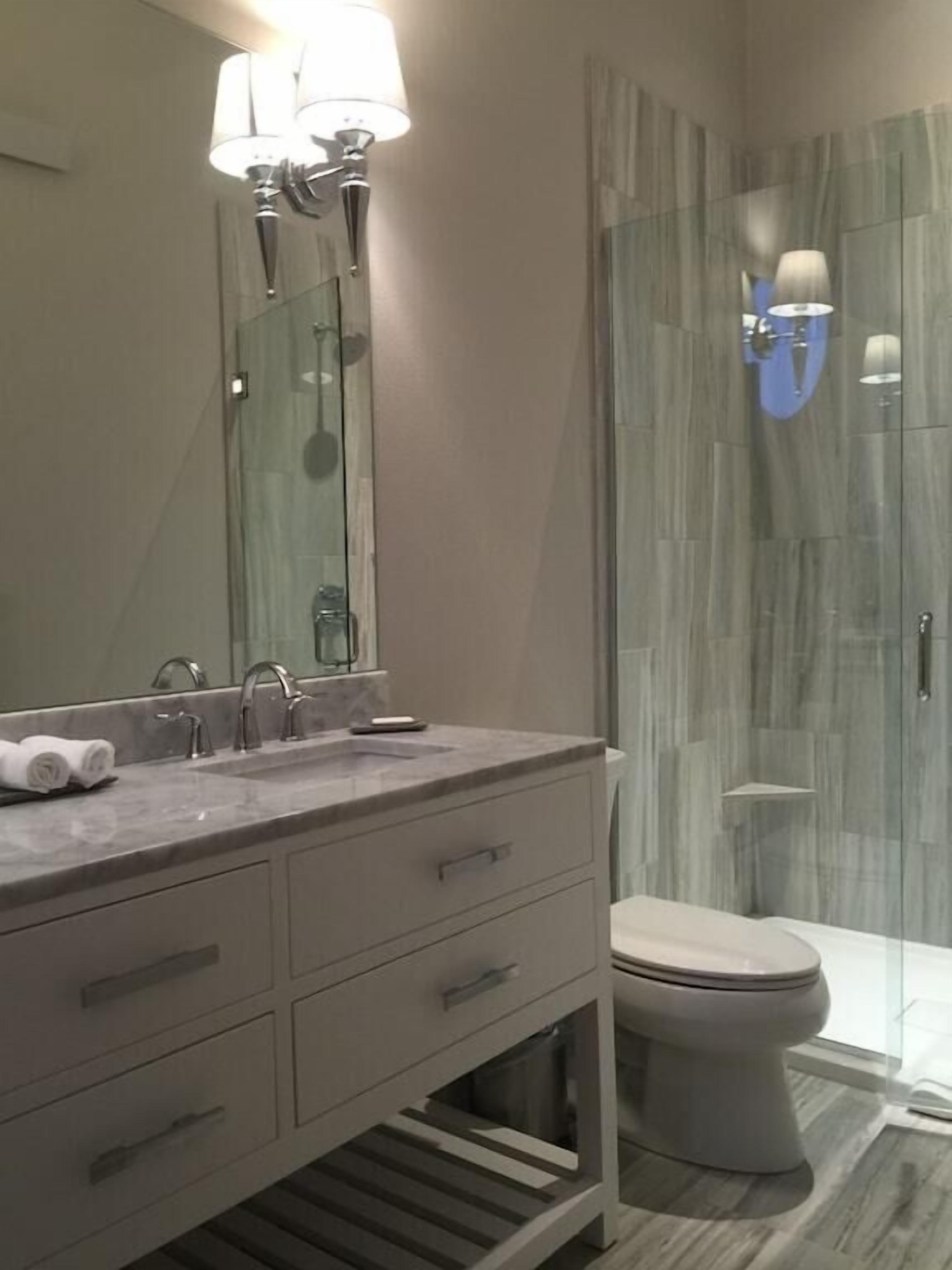 Ein modernes Badezimmer mit Marmorwaschtisch, einem großen Spiegel, Toilette und einer Duschkabine aus Glas.