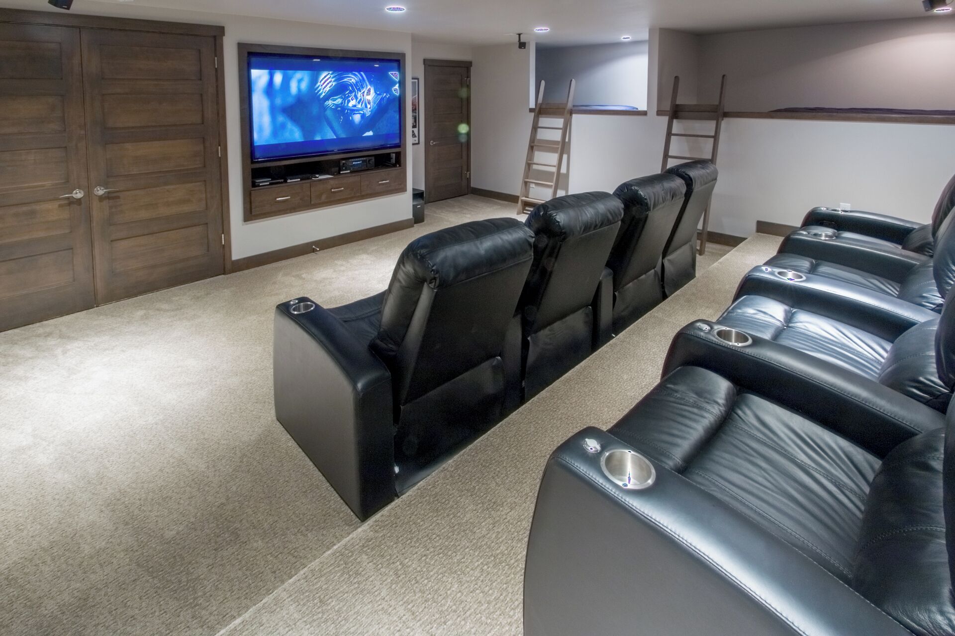 Una sala de cine en casa con una gran televisión de pantalla plana, sillones de cuero reclinables, piso alfombrado y una puerta de madera.