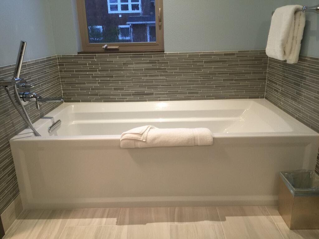 A modern bathroom with a freestanding bathtub, a window above it, and a towel rack on the wall.