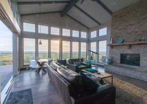 Un salon spacieux doté d’une grande fenêtre donnant sur un paysage naturel, d’une cheminée en pierre et d’un coin salon confortable.