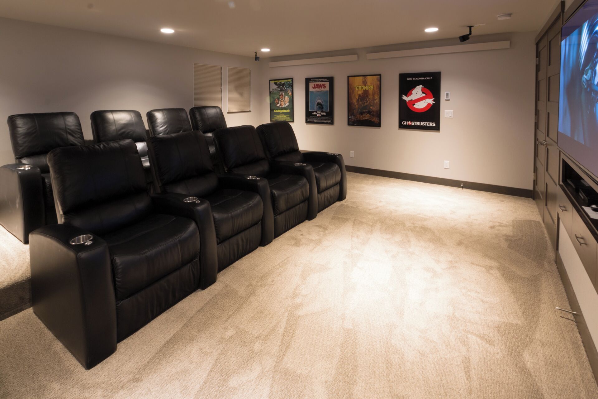 Une salle de cinéma maison avec des fauteuils inclinables en cuir noir, un sol recouvert de moquette et des affiches accrochées au mur.