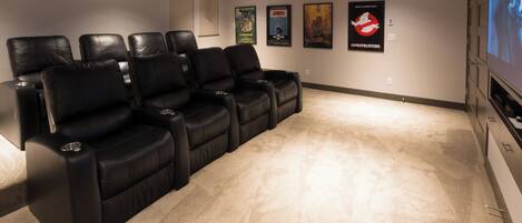 Une salle de cinéma maison avec des fauteuils inclinables en cuir noir, un sol recouvert de moquette et des affiches accrochées au mur.