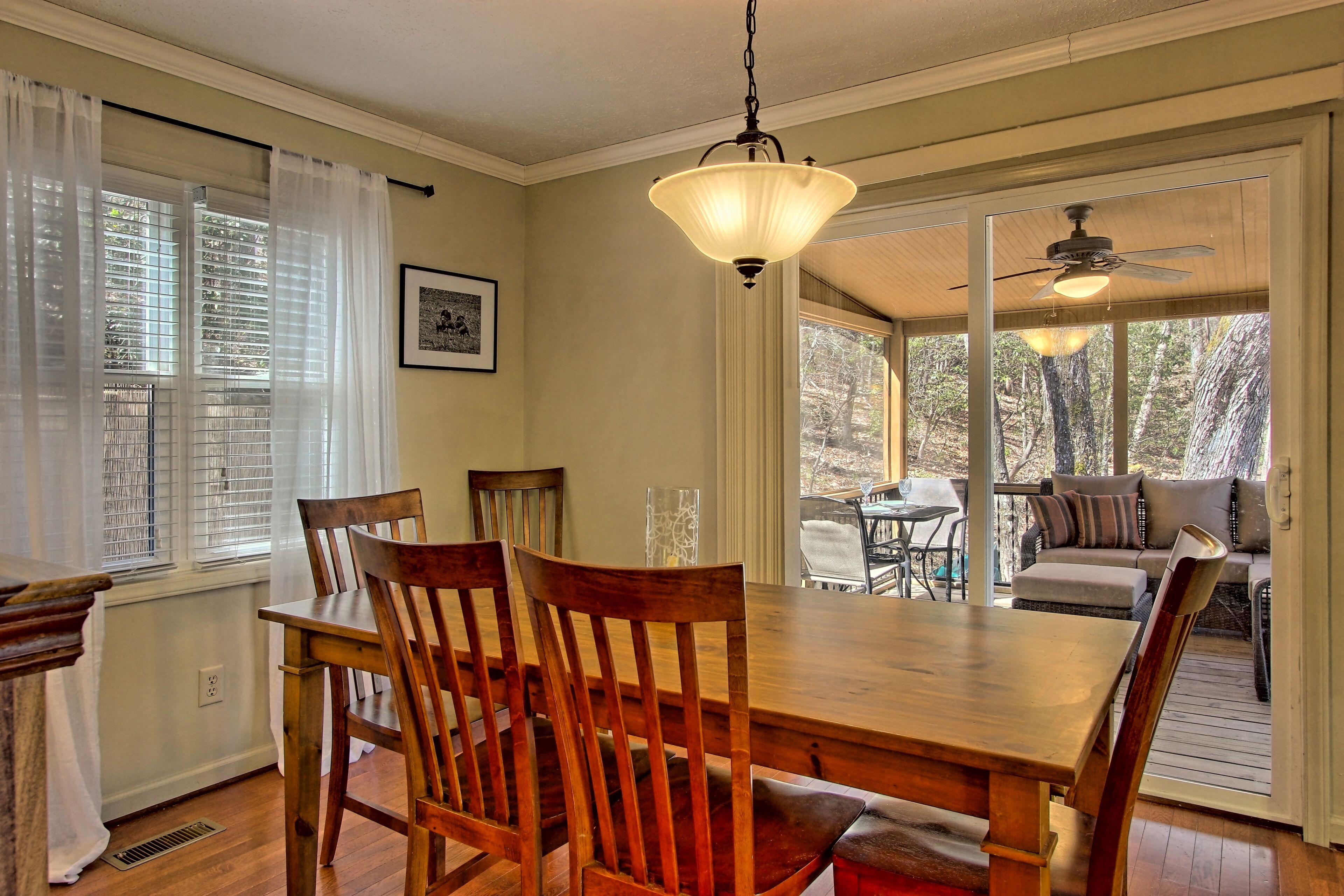 A dining area with a wooden table and chairs, a hanging light fixture, and a view of an outdoor deck.
