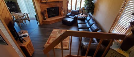 A cozy living room with a fireplace, leather sofa, wooden furniture, and a staircase.