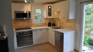 A modern kitchen with white cabinets, stainless steel appliances, a window, and a view of greenery outside.