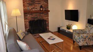 A living room with a brick fireplace, a flat-screen TV, a sofa, a coffee table, and a floral armchair.
