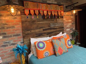 Una habitación con pared de ladrillo, cabecera de madera y cama con almohadas estampadas.