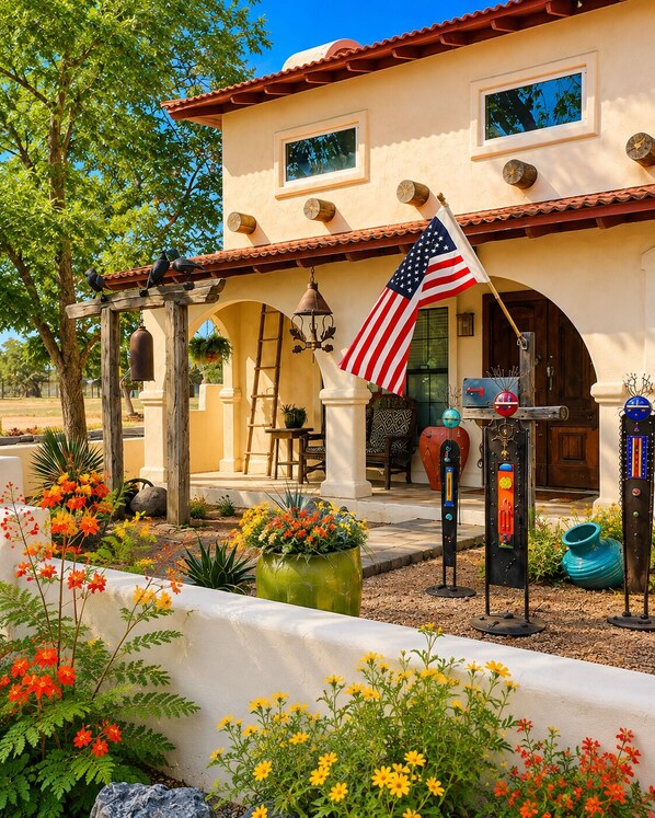 Una casa con un patio, una bandera estadounidense y un jardín lleno de flores coloridas.