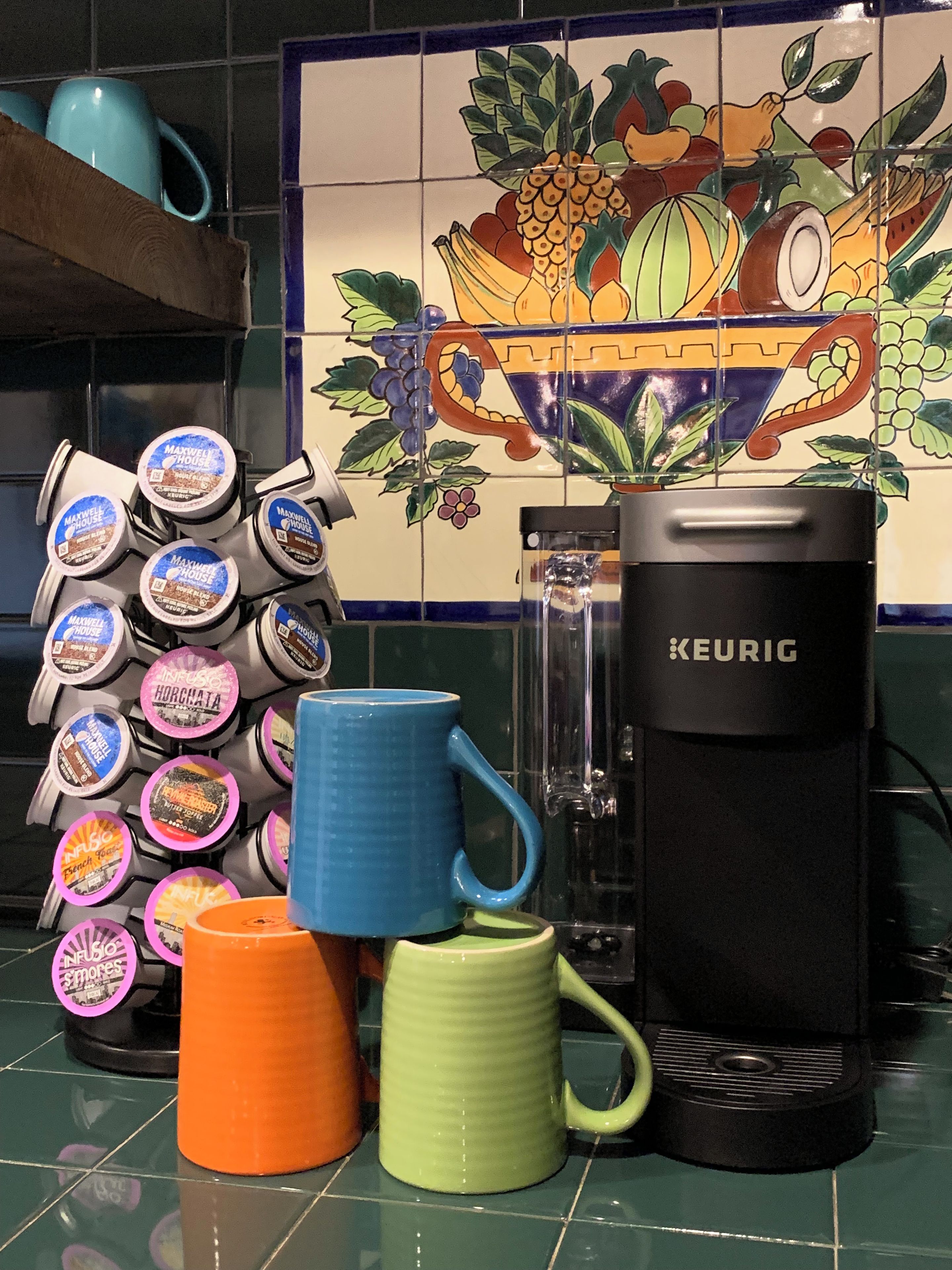 A kitchen counter with a Keurig coffee maker, a stack of coffee pods, and a few mugs.