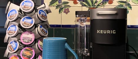 A kitchen counter with a Keurig coffee maker, a stack of coffee pods, and a few mugs.