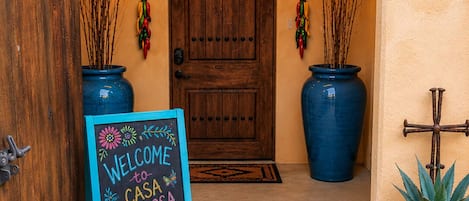 A wooden door with a welcome sign, potted plants, and a decorative wall hanging.
