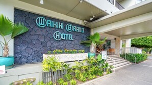 The exterior of the Waikiki Grand Hotel with a stone facade, outdoor seating area, and a sign indicating a full bar. - Oasis in Waikiki w/ Pool ⛱-Steps to the Beach, Zoo, SunDeck Waikiki Grand Hotel® (Honolulu)