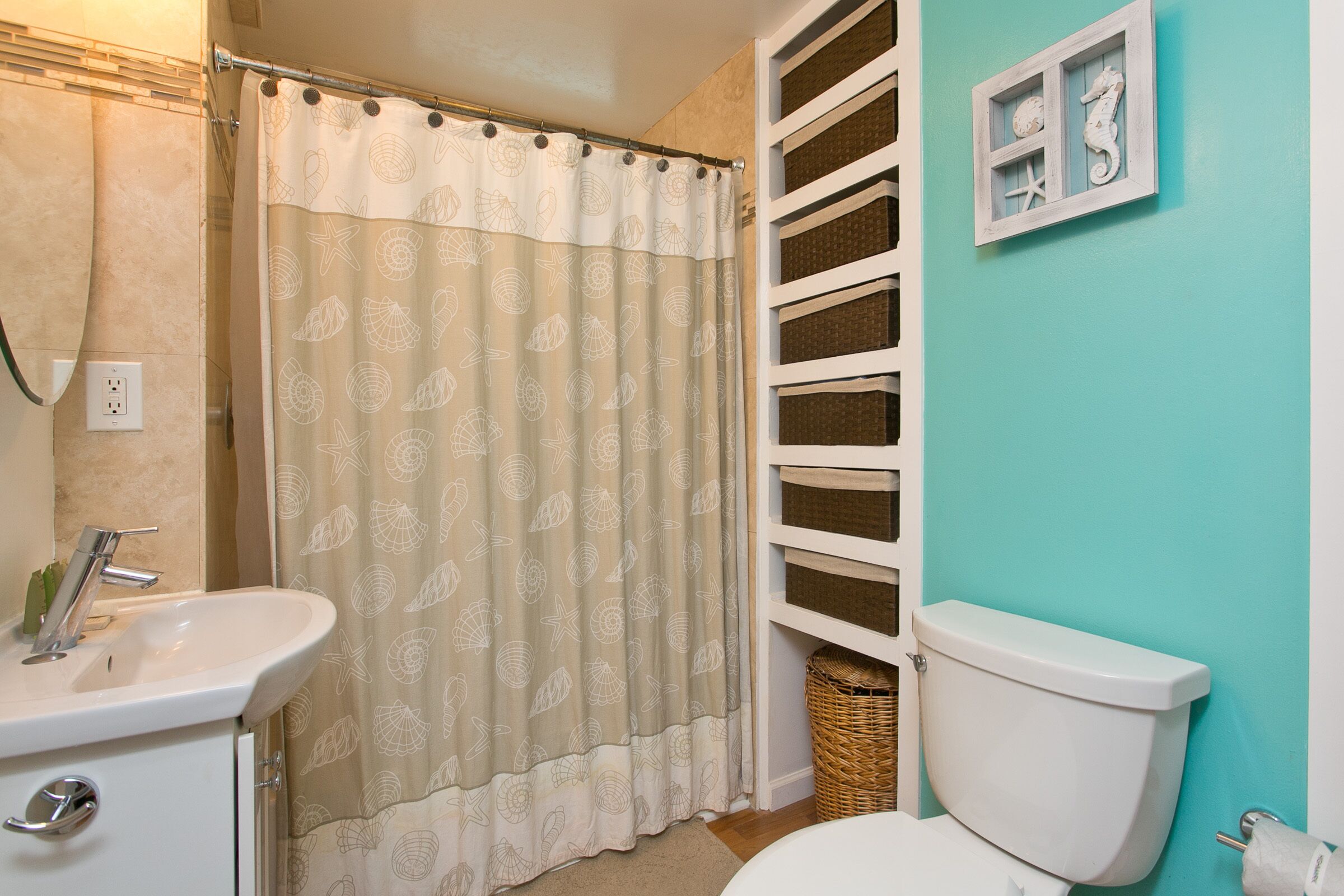 Une salle de bain avec un lavabo blanc, des toilettes et un rideau de douche orné d’un motif de coquillages.