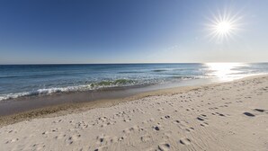 Una spiaggia con impronte che conducono all'acqua, cielo sereno e sole splendente.