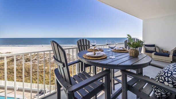 Un balcone con vista sulla spiaggia, un tavolo rotondo con sedie e un'area pranzo.