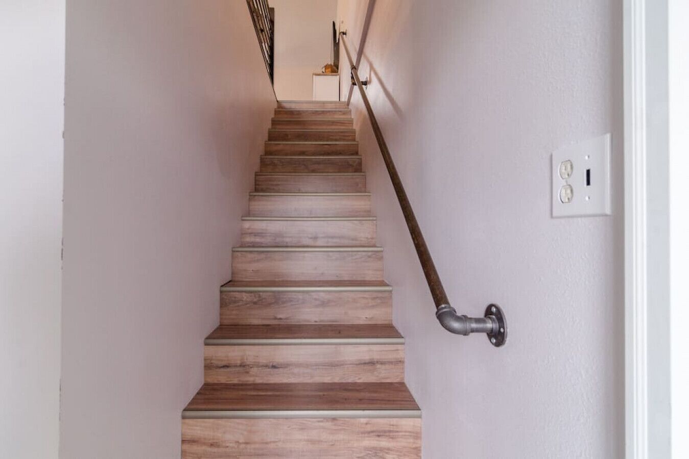 A wooden staircase with a metal handrail and a light switch on the wall.