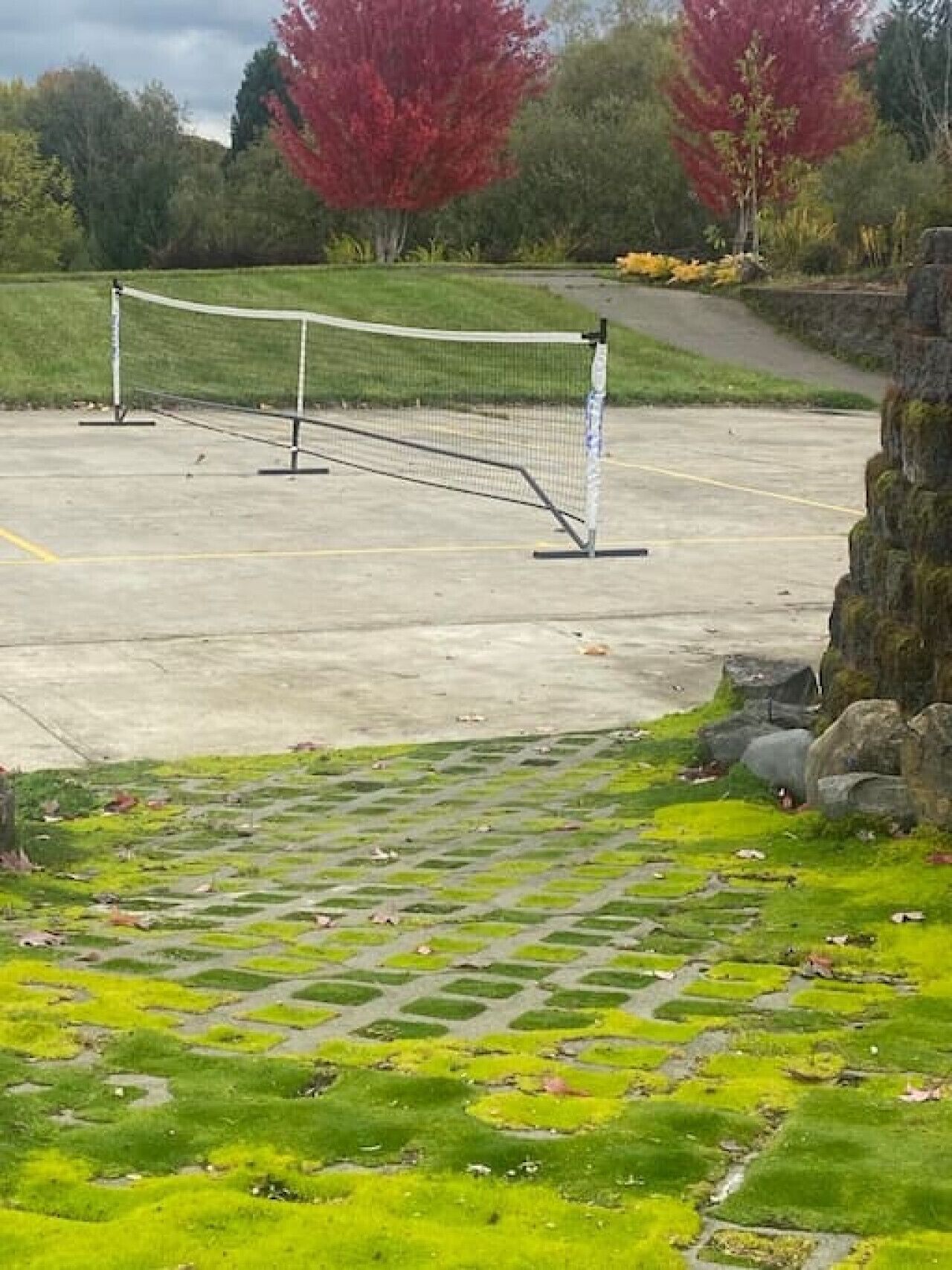 Una cancha de tenis con red, rodeada por un muro de piedra y una zona verde con musgo.