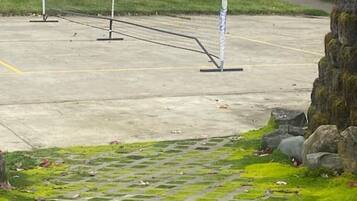 Una cancha de tenis con red, rodeada por un muro de piedra y una zona verde con musgo.