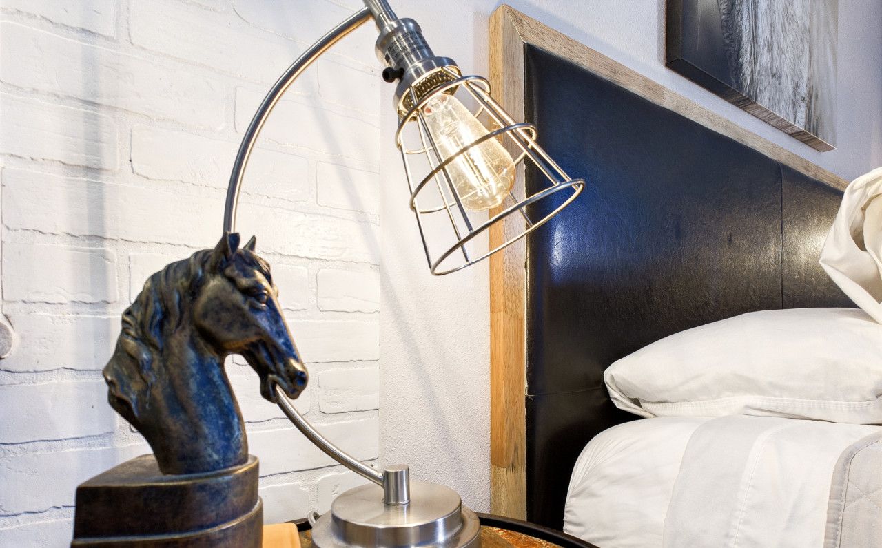A bedroom with a bed, a wooden nightstand, a metal lamp, and a horse statue.