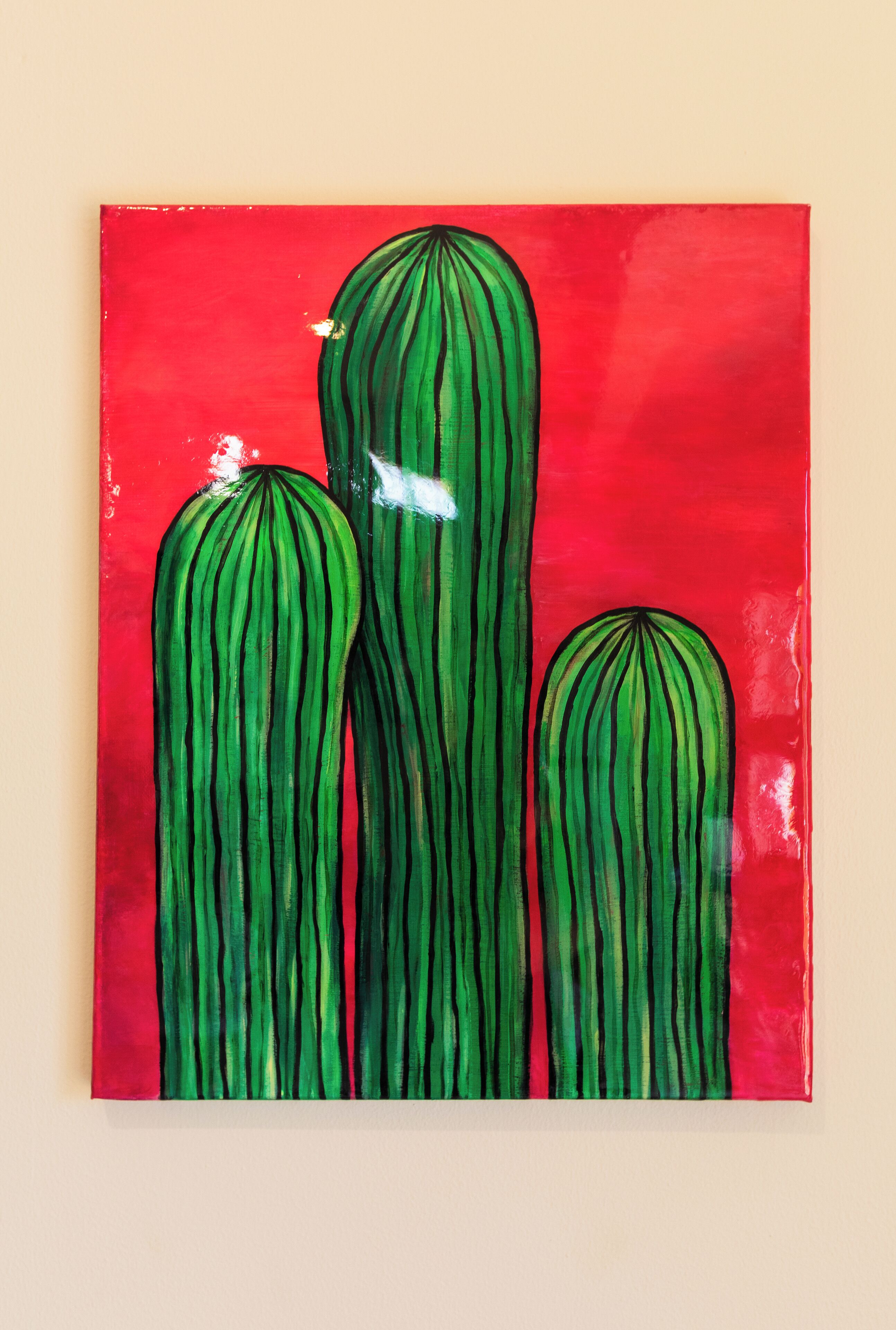 A painting of three cactus plants on a red background.
