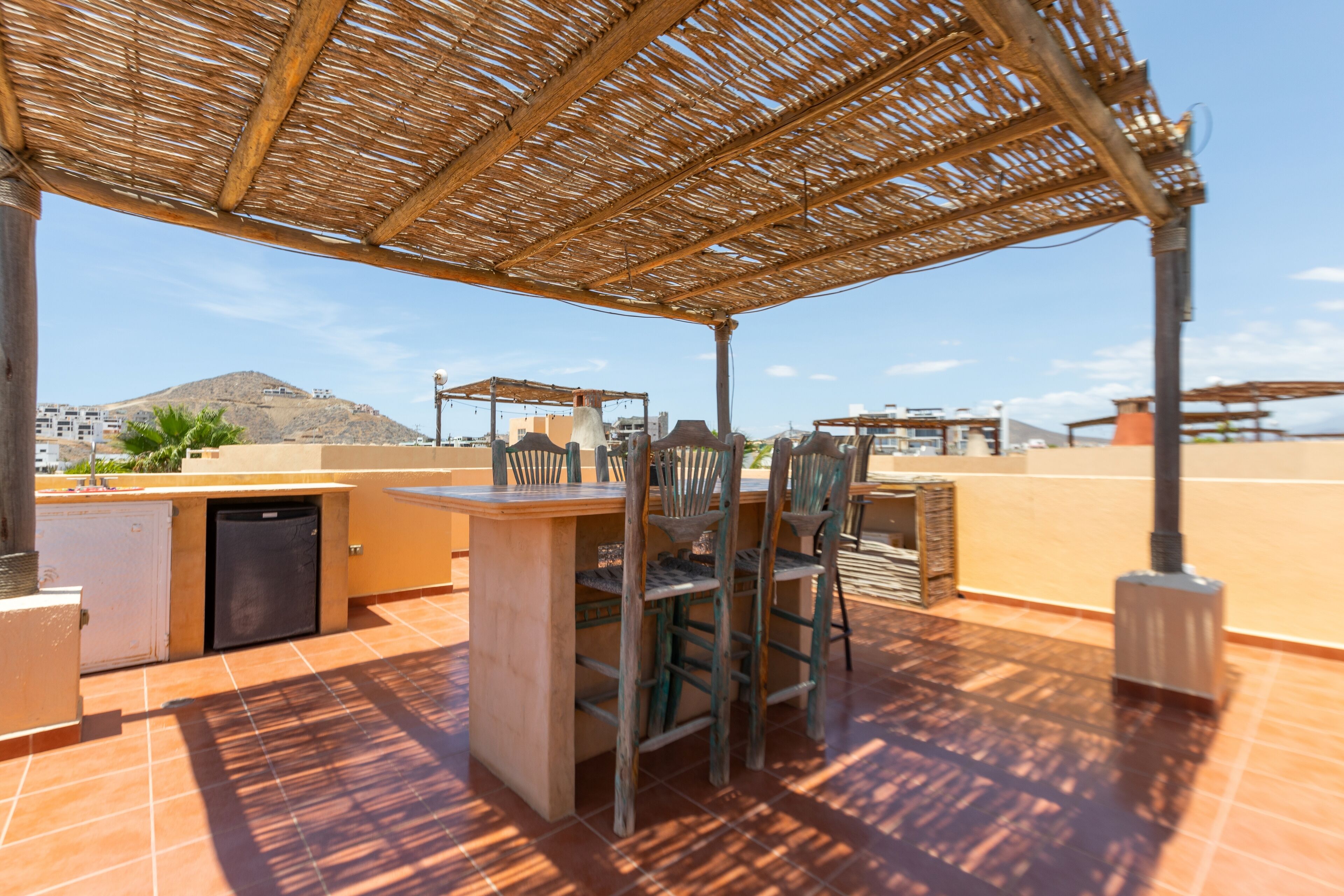 An outdoor patio with a wooden table and chairs, a small kitchen area, and a view of a mountainous landscape.