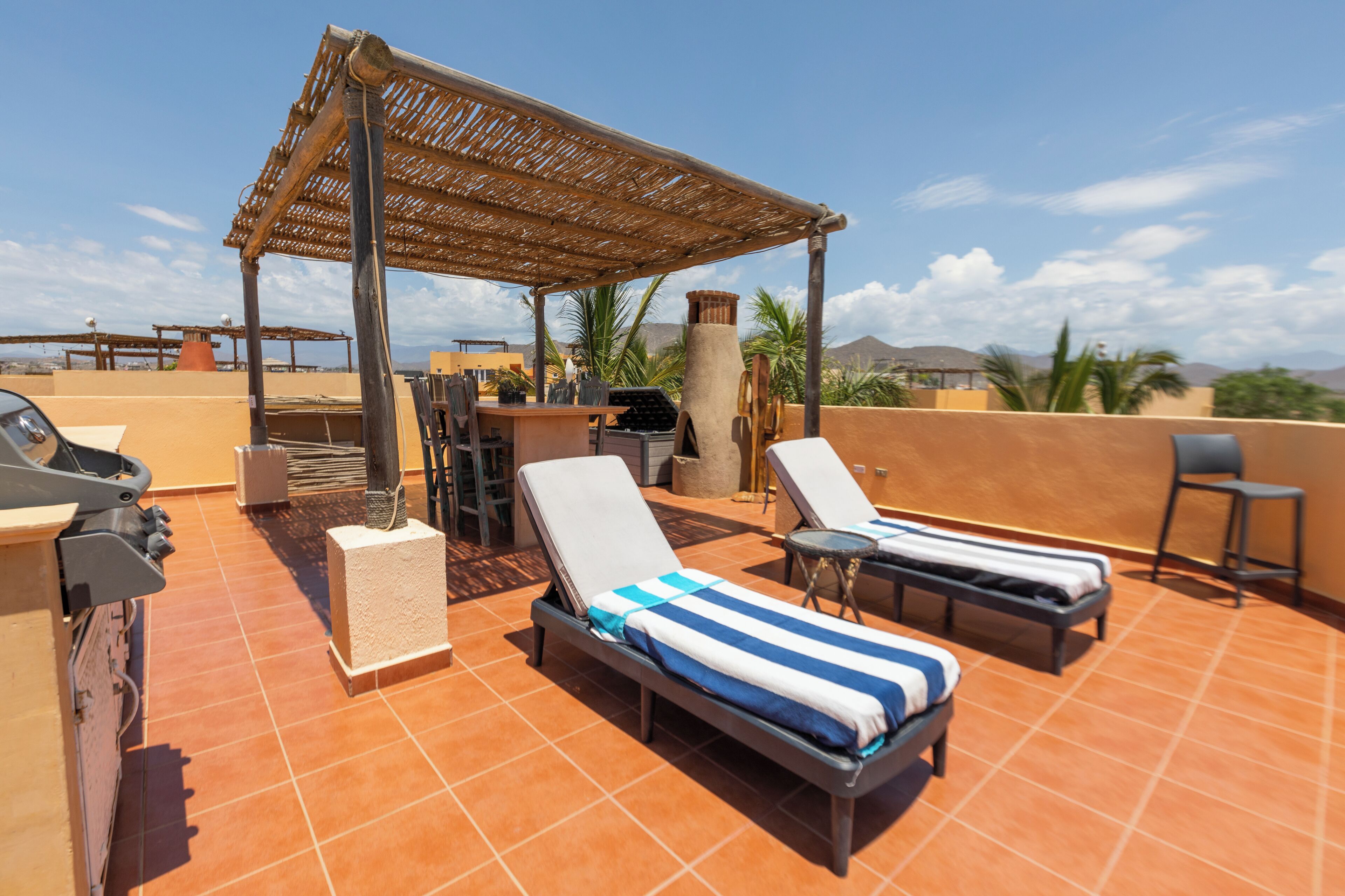A rooftop terrace with two sun loungers, a grill, and a pergola.