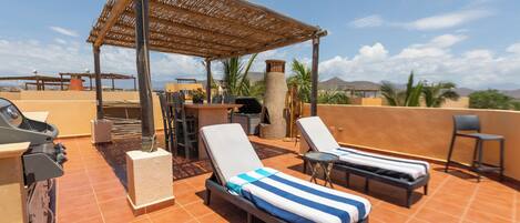 A rooftop terrace with two sun loungers, a grill, and a pergola.