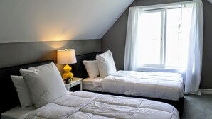 A hotel room with two beds, a nightstand with a lamp, and a window with curtains.