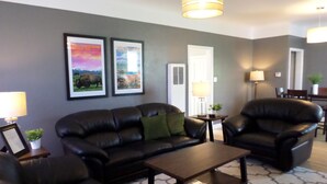 A living room with a dark leather sofa, a matching armchair, a coffee table, and framed pictures on the wall.