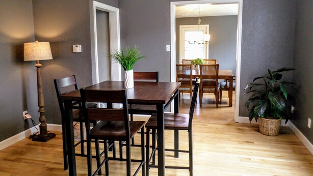 A dining area with a wooden table and chairs, a potted plant, and a lamp.