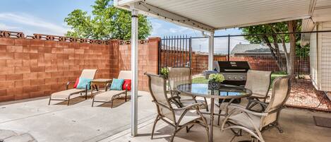 A patio with a covered table and chairs, a grill, and a brick wall.