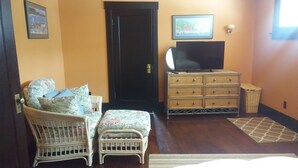 A bedroom with a bed, two wicker chairs, a dresser, a television, and a door.