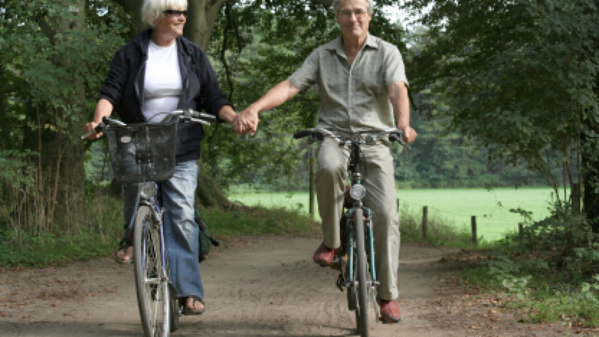 Two people riding bicycles on a dirt path surrounded by greenery.