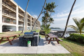 A beachfront hotel with outdoor dining areas, a barbecue grill, and a view of the ocean.