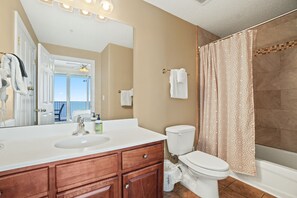 Een badkamer met een witte wastafel, een houten wastafelmeubel, toilet en douchegordijn.