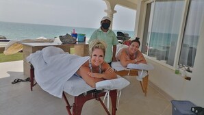 Une salle de massage avec vue sur l’océan, une table de massage, un massothérapeute et un patient.