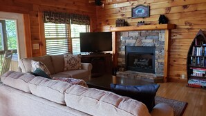 A cozy cabin interior with a stone fireplace, wooden walls, a sofa, and a television. - Breathtaking views from decks! Private acres next door to Dollywood! Beautiful! (Pigeon Forge)