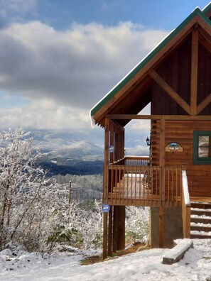 A wooden cabin with a balcony, surrounded by snow-covered trees and mountains in the background. - Breathtaking views from decks! Private acres next door to Dollywood! Beautiful! (Pigeon Forge)