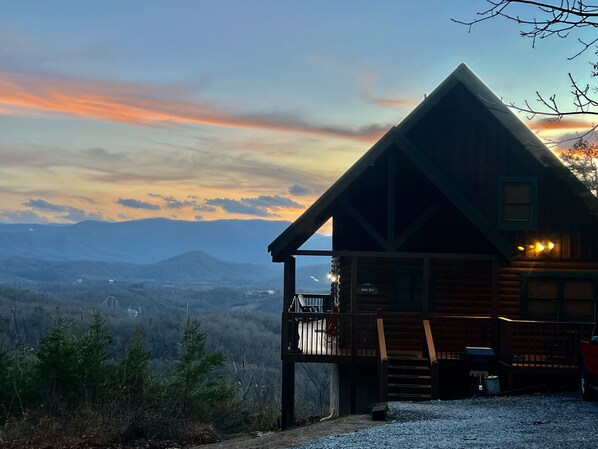 Una cabaña con balcón que da a un paisaje montañoso al atardecer.