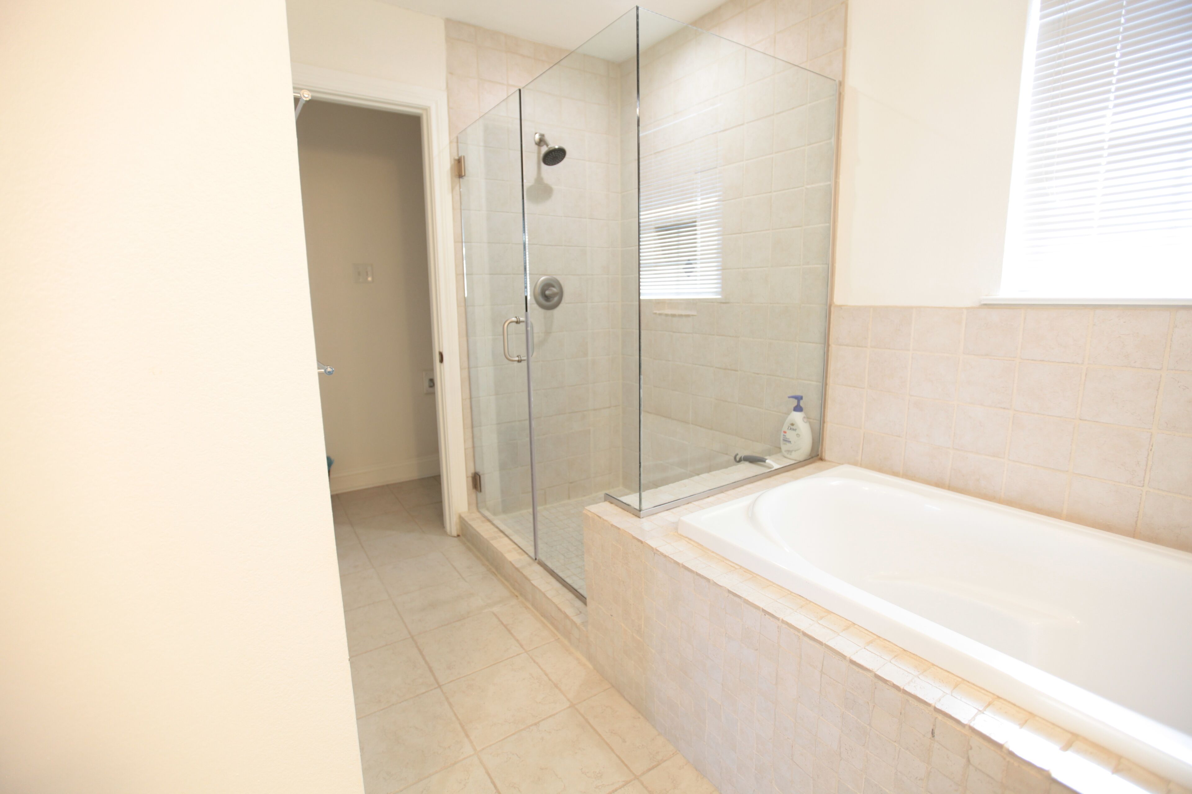 Un bagno con cabina doccia in vetro, una vasca da bagno bianca e pareti rivestite di piastrelle color beige.