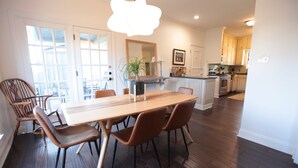 Een eetgedeelte met een houten tafel en bruine stoelen, een keuken met houten keukenkastjes, en een groot raam met uitzicht.