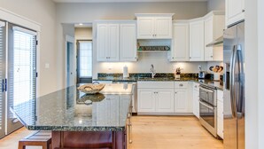 A modern kitchen with white cabinets, a granite countertop, stainless steel appliances, and a built-in island with a bowl. - 4BR townhome near the beach with parking, WiFi, and pet-friendly stays. (Virginia Beach)