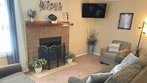 Un salon avec une cheminée, un téléviseur fixé au mur et un ensemble de canapés.
