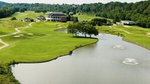 Un parcours de golf avec un étang, un club-house et une forêt environnante.