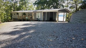 A single-story house with a covered porch, a gravel driveway, and a view of a body of water. - Newly Renovated Lakeside Cottage, Beautiful Lake Views With Adjacent Boat Ramp. (Dover)