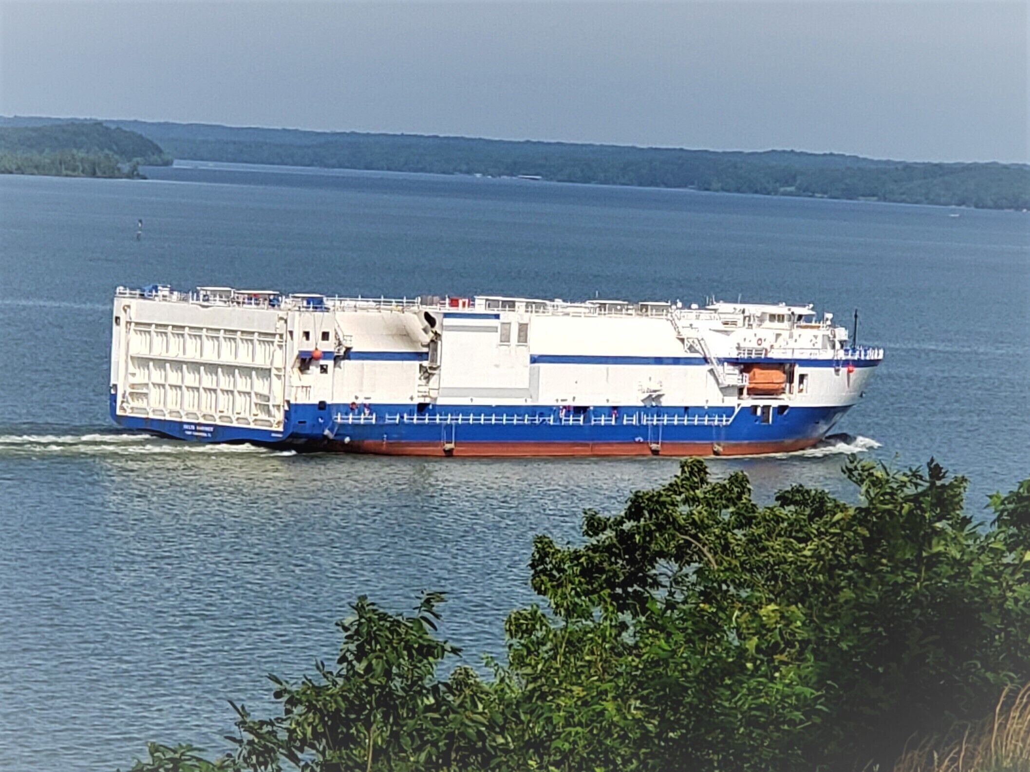 Un grand navire de croisière à plusieurs ponts, aux couleurs bleu et blanc, naviguant sur une étendue d’eau calme.