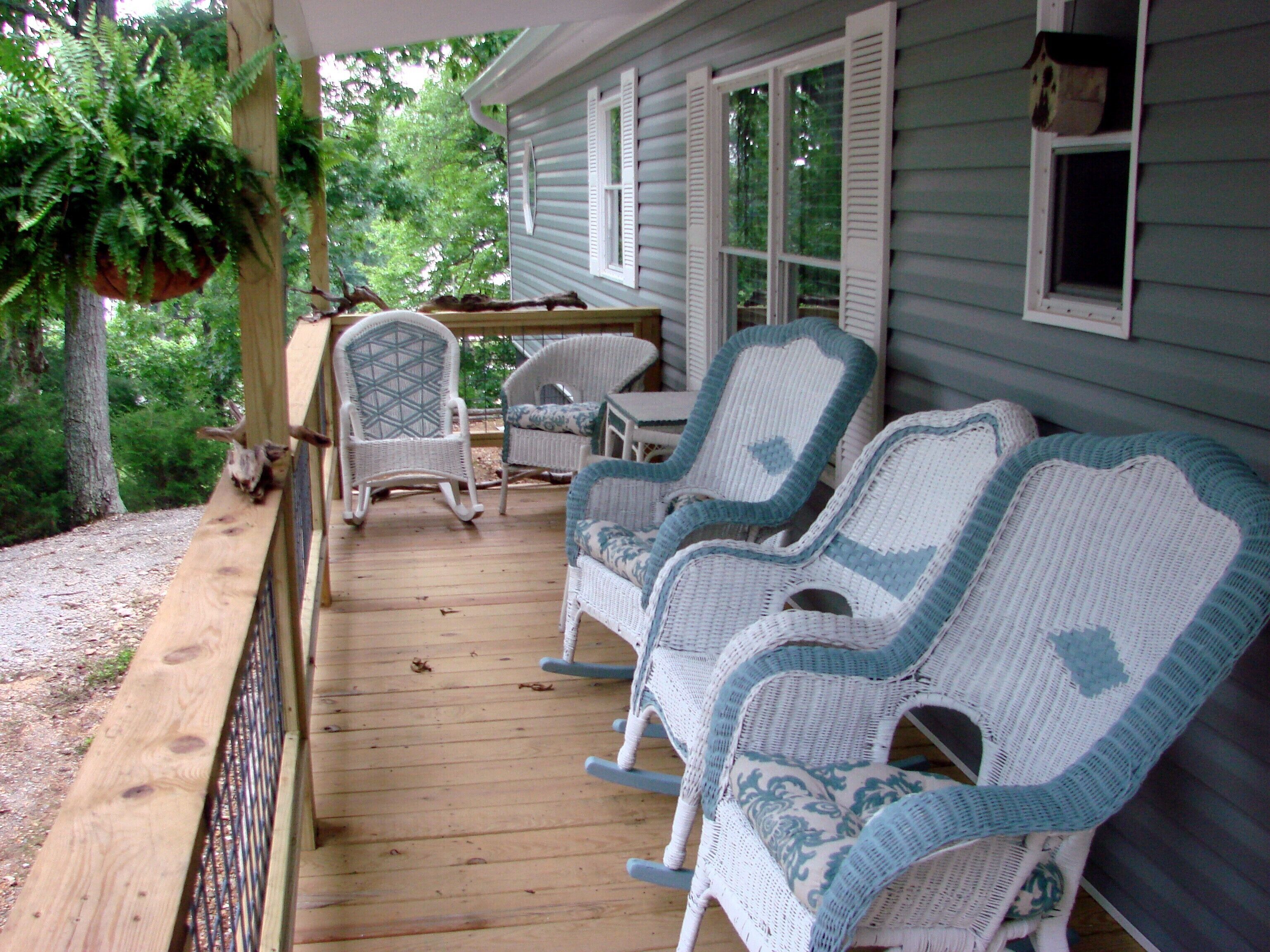 A covered porch with wicker chairs and a table, surrounded by trees.